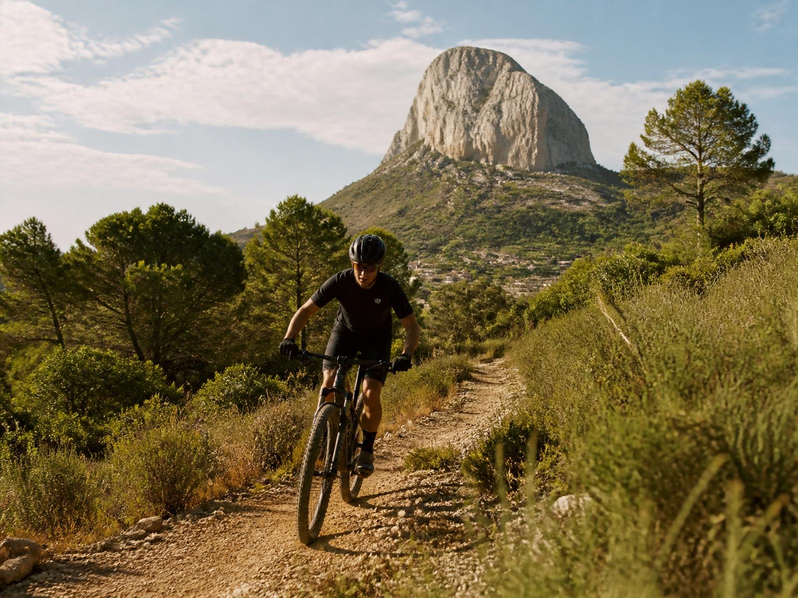 Ciclista de BTT en sendero de la Vall de Pop, con el Penyó al fondo