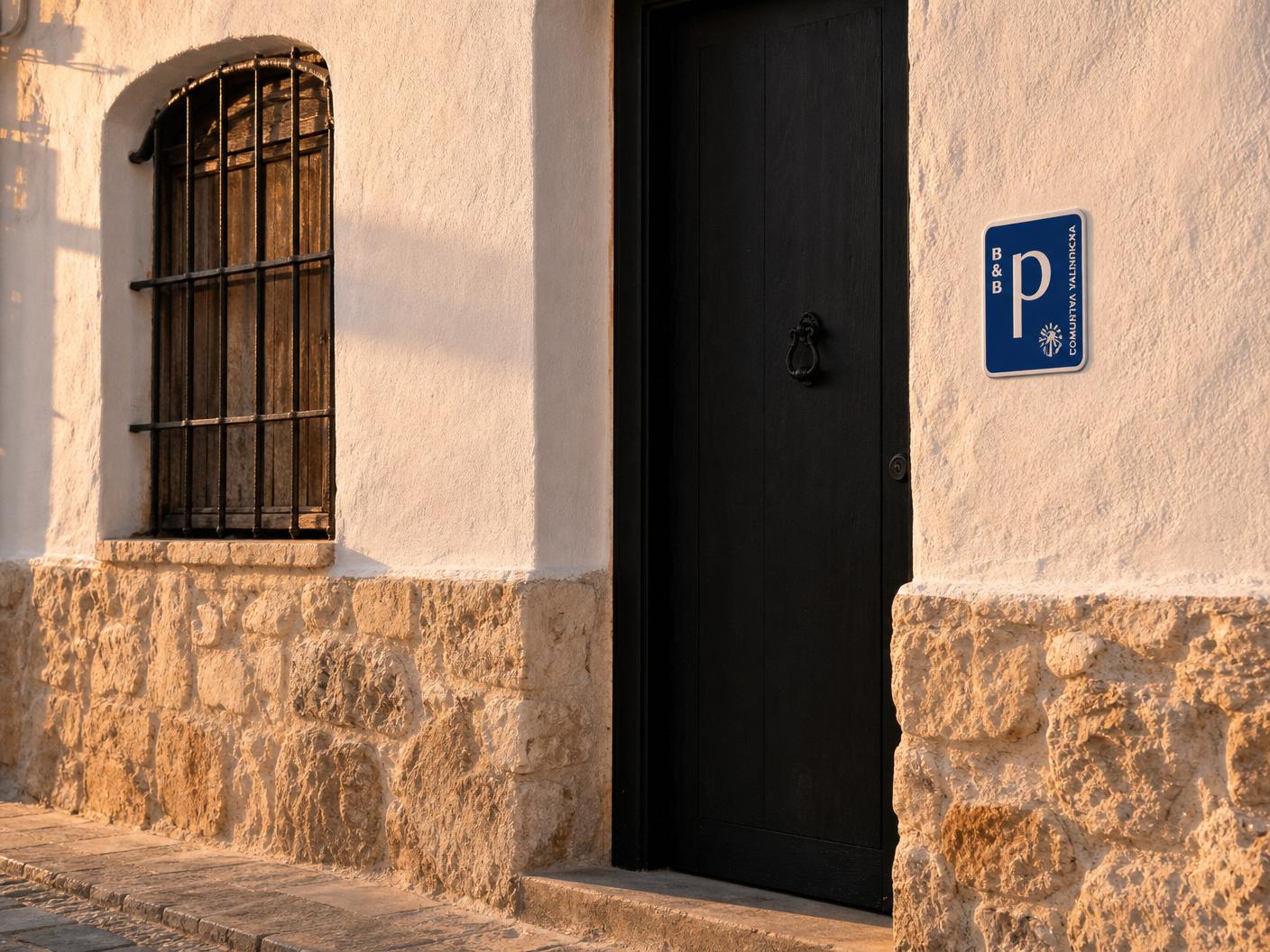 Piedra, cal y hierro en la fachada Detalle de la fachada de Purissima House: zócalo de piedra, muro encalado, reja de hierro y la puerta de entrada a primera hora